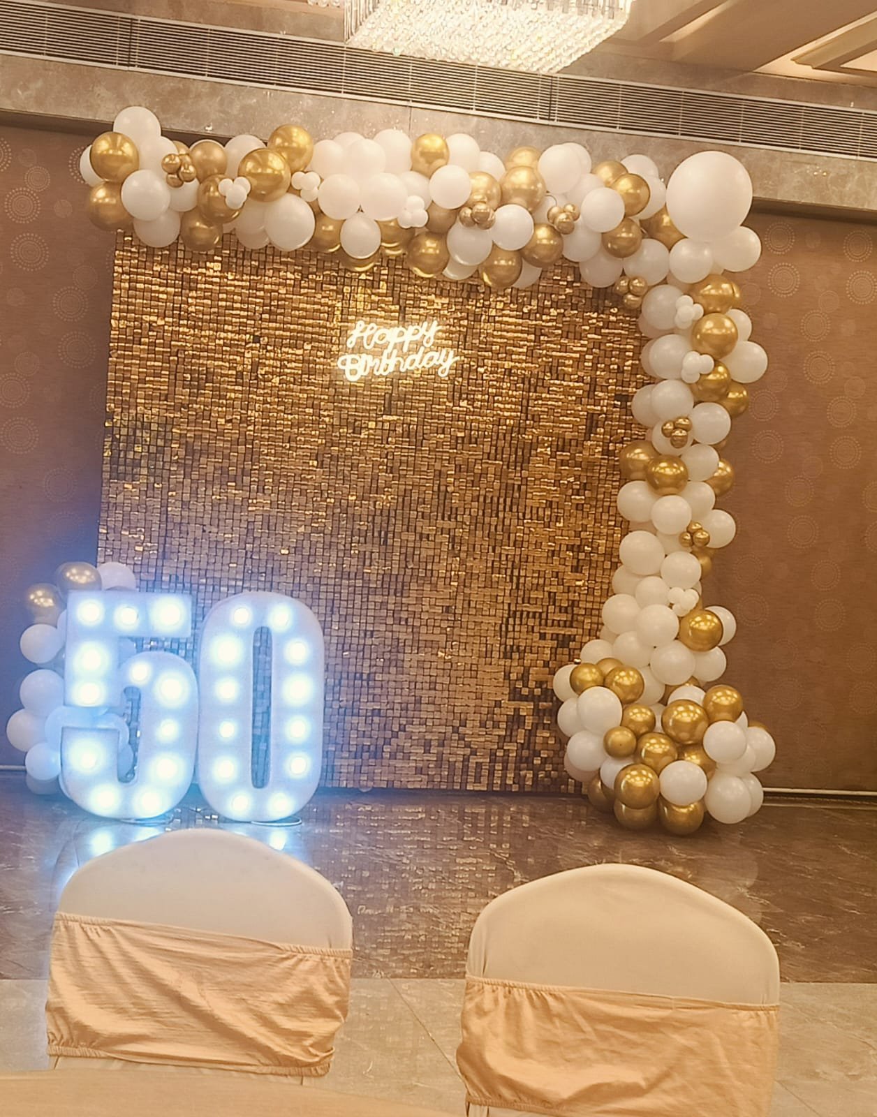 Gold sequin wall with white and gold balloon garland and marquee numbers